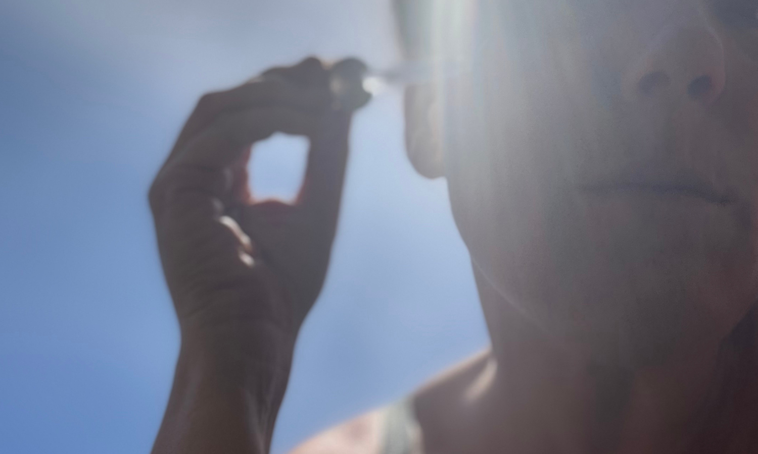 Sun in the background and dropper of skin serum going on a face